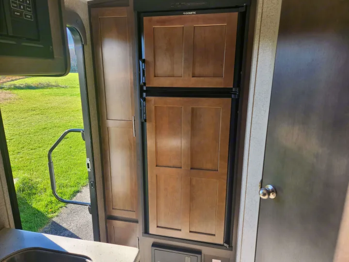 Inside an RV rental: kitchen space with Dometic fridge, cabinet, and an open door revealing a sunny green field.. Forest River Rockwood Mini Lite 2019