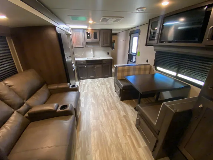 This rv rental interior features a cozy living area with a recliner, a well-equipped kitchen, and a dining booth.. Grand Design Transcend 2021