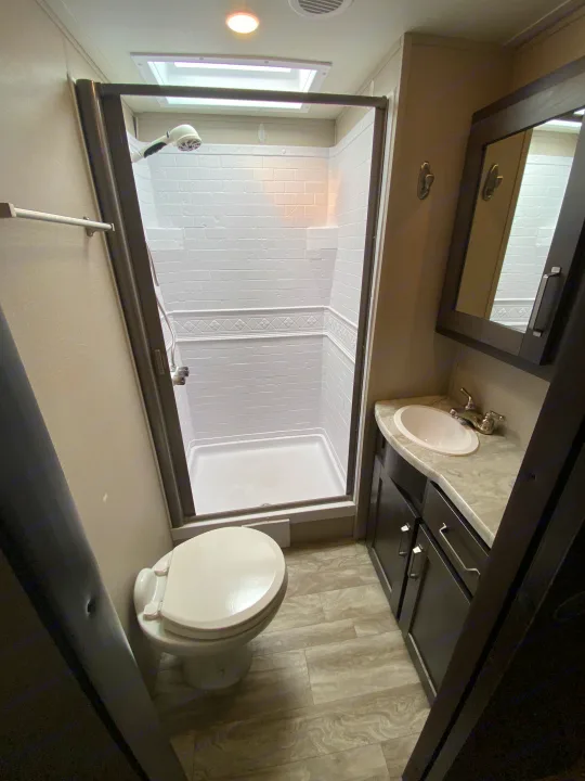 Clean RV rental bathroom with a glass shower, toilet, and vanity sink, featuring modern finishes and ample light.. Grand Design Transcend 2021