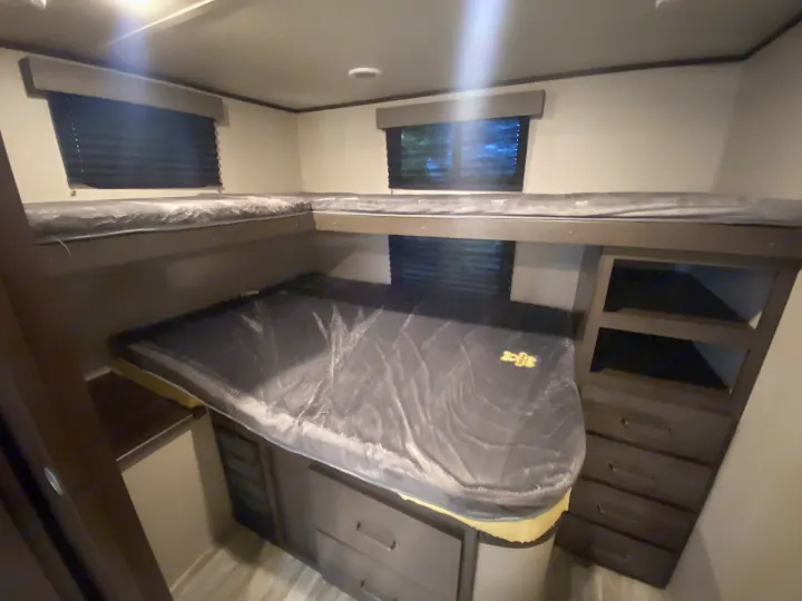 RV rental interior featuring a comfortable L-shaped bunk bed with an upper bunk, privacy blinds, and built-in drawer storage.. Grand Design Transcend 2021