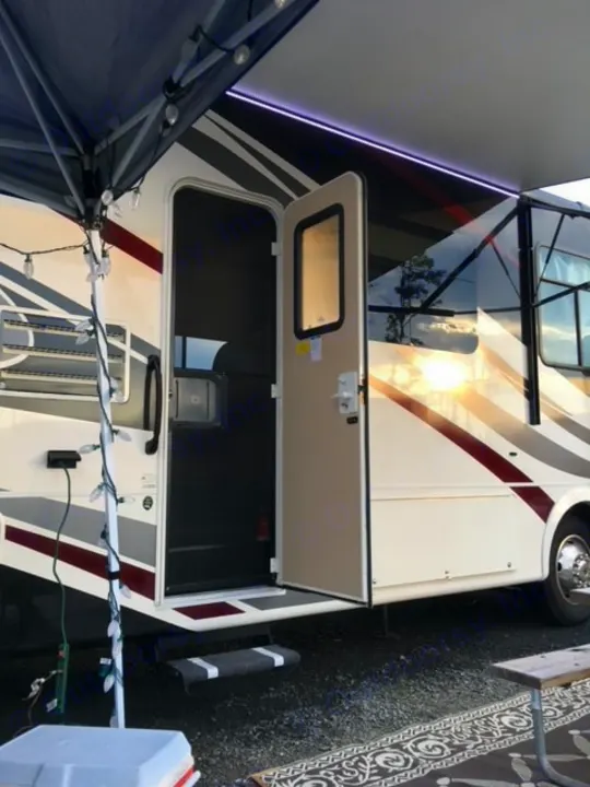 This RV rental's campsite setup features an extended awning with LED lights, inviting open door, and string lights.. Forest River Coachmen Pursuit 2017