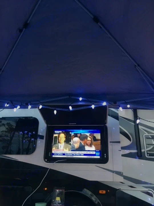 RV rental with an exterior TV showing news, set up under a blue canopy adorned with string lights for outdoor entertainment.. Forest River Coachmen Pursuit 2017