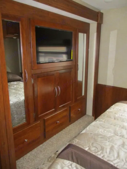 RV rental interior: cozy bedroom with built-in TV, ample wooden storage, and comfortable bedding.. Forest River Coachmen Pursuit 2017