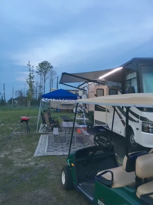 RV rental campsite at dusk: an RV with lit awning, outdoor living area, & golf cart are ready for relaxation.. Forest River Coachmen Pursuit 2017