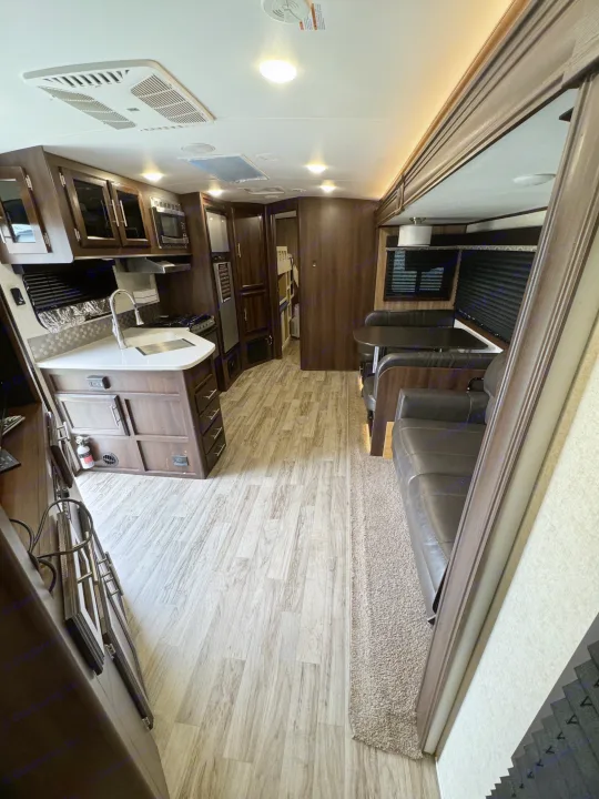 Explore this modern RV rental interior: a full kitchen, dining booth, comfy sofa, and bunk area with light wood-look floors.. Jayco White Hawk 2018