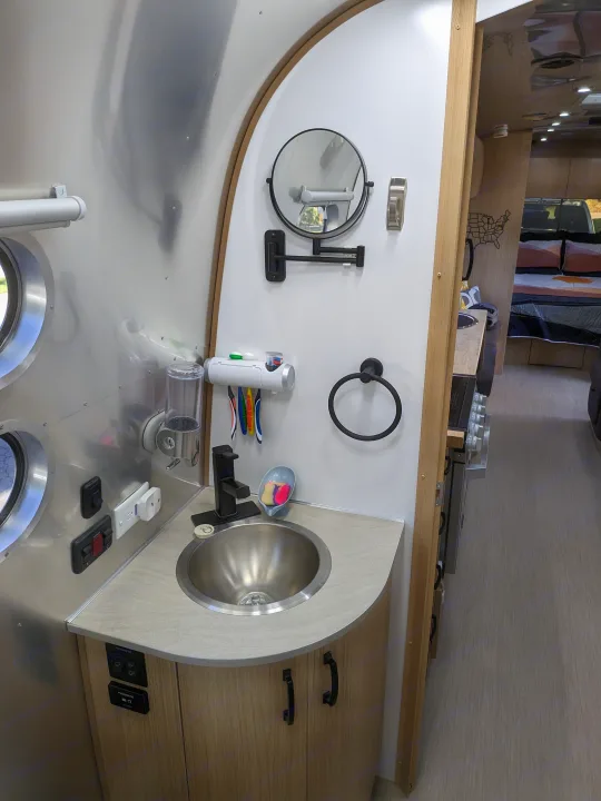 Inside an RV rental: a modern, compact bathroom vanity featuring a stainless steel sink, black faucet, and mounted mirror.. Airstream Flying Cloud 2020