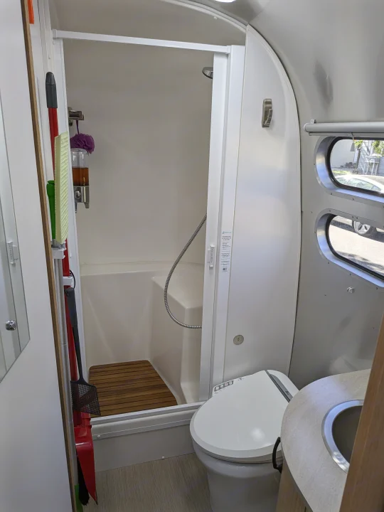 RV rental's compact bathroom: shower with a wooden mat, smart toilet, and sink. Space-saving design for travel.. Airstream Flying Cloud 2020