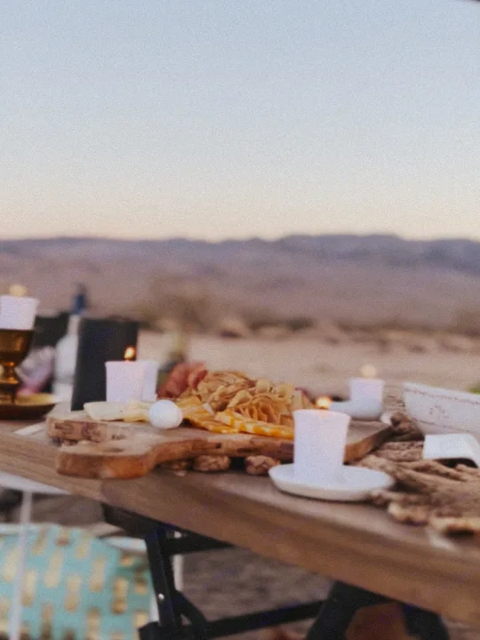 RV rental glamping: A cozy charcuterie board with lit candles on a wooden table, set against a blurred desert mountain backdrop at dusk.. Ford E450 1999