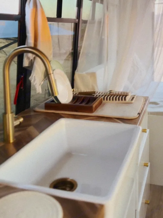 Compact kitchen in an RV rental, featuring a white sink, gold faucet, and dish drying rack. Ideal for mobile living.. Ford E450 1999