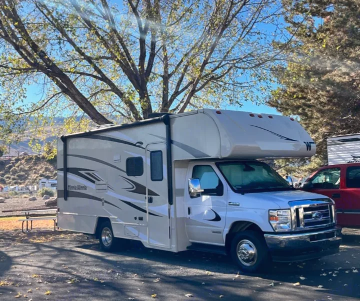 White Winnebago Minnie Winnie Class C RV rental parked under a tree in a sunny RV park setting.. Winnebago Minnie Winnie 2022