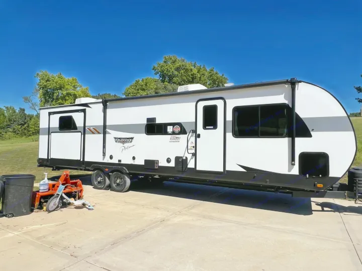 A white Wildwood Platinum travel trailer, ideal for an RV rental, parked on concrete under a clear blue sky.. Forest River 31KQBTS 2024