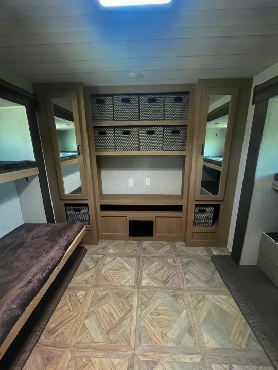 RV rental bunkhouse area with comfortable bunk beds, central storage unit holding woven bins, and patterned floor.. Forest River 31KQBTS 2024