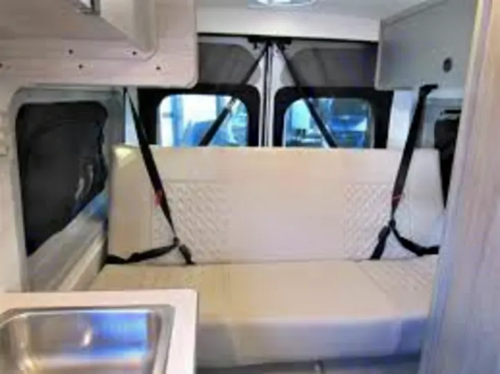 Inside an RV rental camper van, showing a white rear bench seat with seatbelts & a small sink area.. Winnebago Solis 2022