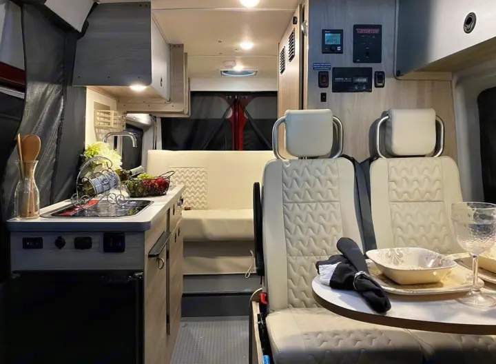 Modern RV rental interior: compact kitchen, swiveling front seats, and a comfortable rear bench.. Winnebago Solis 2022