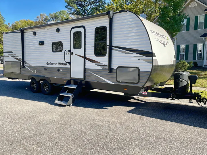 A white Starcraft Autumn Ridge travel trailer, an RV rental, parked on asphalt with its entry steps deployed.. Starcraft Autumn Ridge 2023