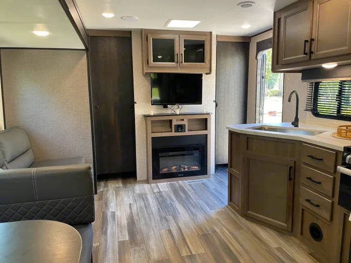 Inviting RV rental interior: cozy living space with a grey sofa, TV & fireplace, plus a sleek kitchen with sink & cabinetry.. Starcraft Autumn Ridge 2023
