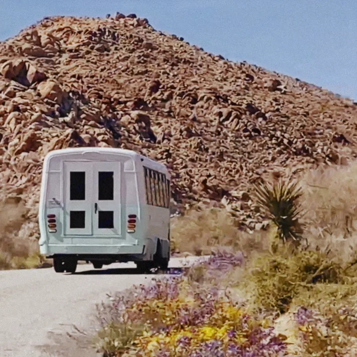 A light-colored RV rental bus drives on a desert road past rocky hills and vibrant wildflowers. Ideal for your desert road trip.. Ford E450 1999
