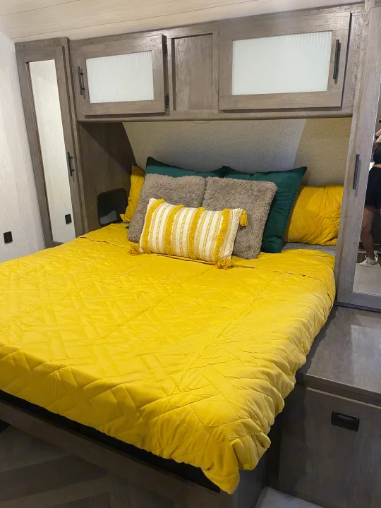 Cozy RV rental bedroom with a bed, bright yellow comforter, and decorative pillows, plus overhead storage.. Forest River Salem 2022