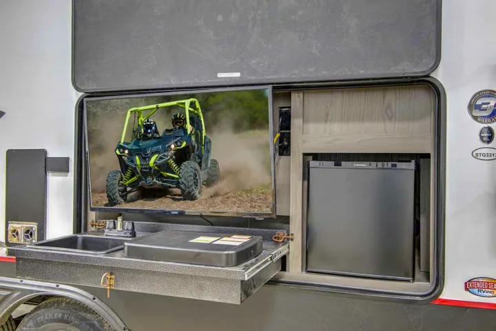 RV rental with outdoor kitchen: TV displaying UTV action, sink, griddle, & mini-fridge for ultimate outdoor convenience.. Cruiser Rv Corp Stryker 2022