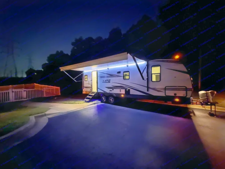 Brightly lit white travel trailer RV rental at night, featuring a deployed awning with blue LED lights and inviting steps.. Cruiser RV MPG Ultra Lite 2022