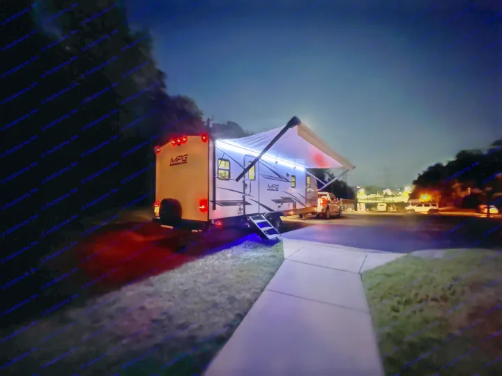 A white RV rental is brightly lit at night with blue awning lights and glowing red taillights, ready for camping.. Cruiser RV MPG Ultra Lite 2022