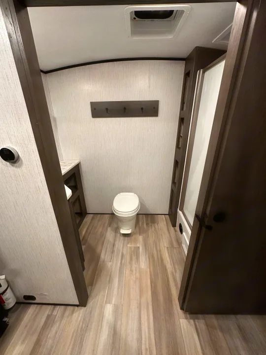 Inside an RV rental, this modern bathroom features a toilet, shower enclosure, small vanity, and light wood-look flooring.. Cruiser RV MPG Ultra Lite 2022