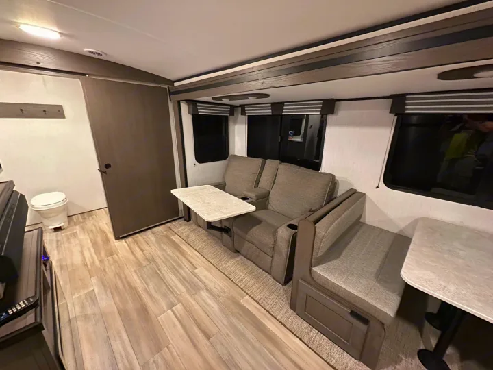 Experience a modern **rv rental** interior: light wood-look flooring, comfy recliners with tables, dinette, and bathroom access.. Cruiser RV MPG Ultra Lite 2022