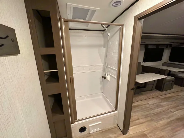 Inside an rv rental: a pristine shower stall with glass door, built-in shelving, and a bright dinette area.. Cruiser RV MPG Ultra Lite 2022