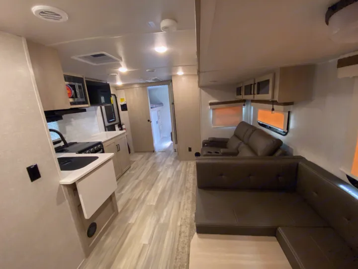 Bright rv rental interior: modern kitchen, large L-shaped sofa, and cozy reclining seats in a spacious living area.. Forest River Rockwood 2023