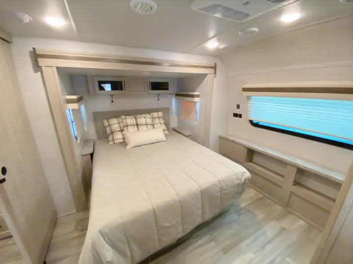 This inviting RV rental bedroom offers a comfortable bed, overhead cabinets, and built-in storage, ideal for compact travel.. Forest River Rockwood 2023