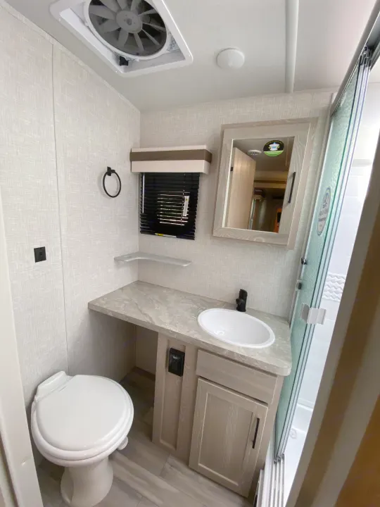 Clean & modern RV rental bathroom. Features a compact toilet, vanity with sink, black faucet, mirror, & shower.. Forest River Rockwood 2023