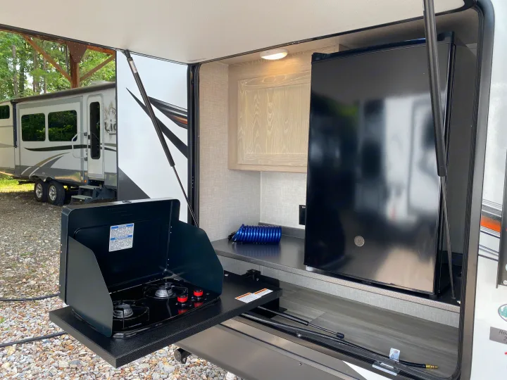 An RV rental's outdoor kitchen features a gas stove, mini-fridge, and counter, perfect for convenient camping and cooking.. Forest River Rockwood 2023