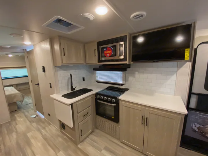 Modern RV rental kitchen with microwave, stove, sink, and bedroom view, perfect for road trips.. Forest River Rockwood 2023