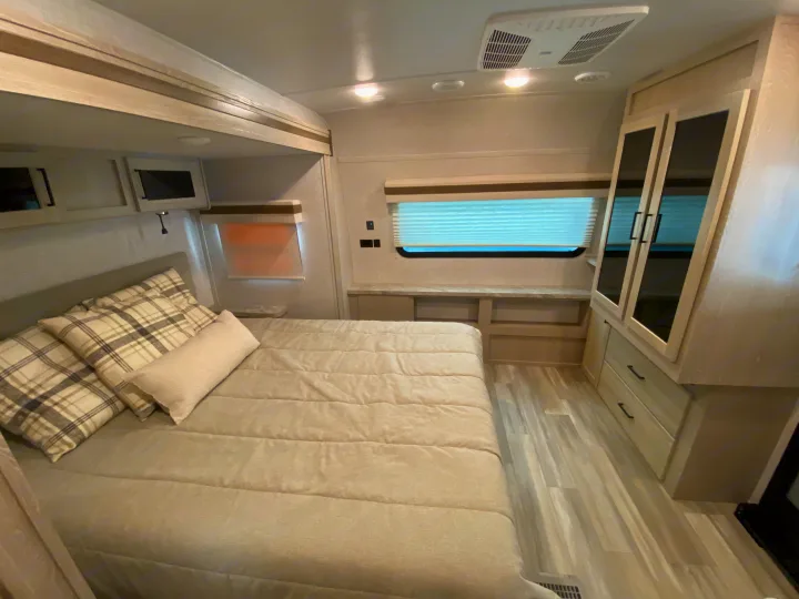 Modern RV rental bedroom featuring a comfortable bed, overhead cabinets, and bright windows, ideal for travel comfort.. Forest River Rockwood 2023