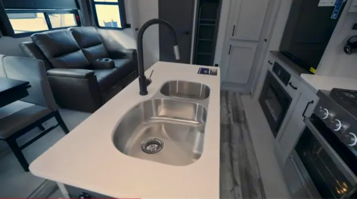 Spacious rv rental interior features a kitchen island with double sink, oven, reclining sofa, and dining space.. Keystone RV Montana High Country 2023
