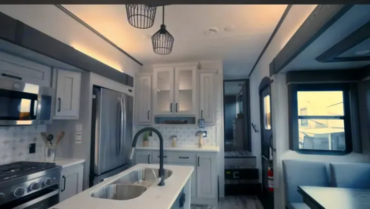 This modern RV rental interior features a spacious kitchen with stainless steel appliances, an island, and a cozy dining area.. Keystone RV Montana High Country 2023
