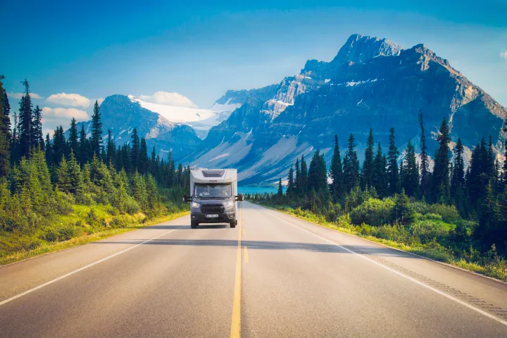 An RV rental journeys through Canada's scenic Rockies, passing a blue lake, dense forests, and majestic snow-capped peaks.. PILOTE A696G Atlas 2025