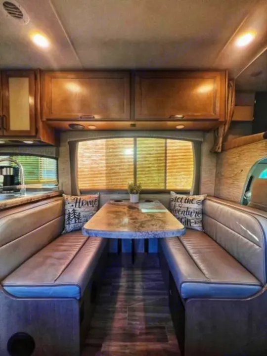 Step inside this RV rental's cozy dinette, featuring two upholstered benches, a table, and overhead storage cabinets.. Thor Four Winds 2022