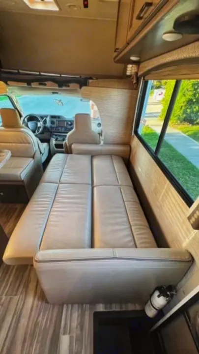 Spacious RV rental interior featuring a beige convertible dinette bed, front cockpit, and wood flooring.. Thor Four Winds 2022
