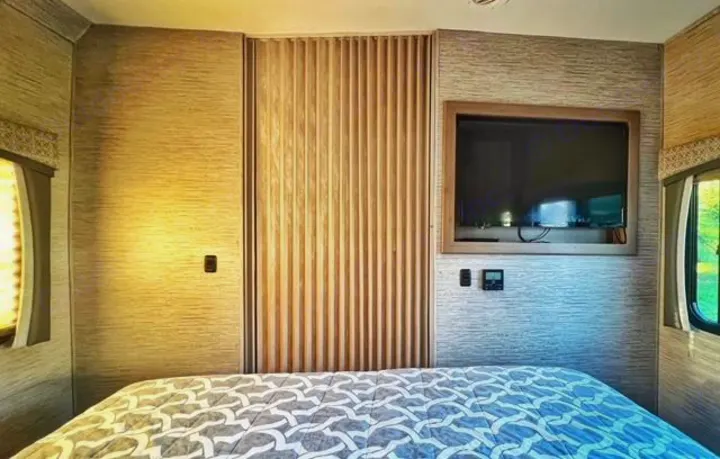 Inside a comfortable **RV rental**: A bedroom with a patterned bed, wall-mounted TV, and a unique wooden slatted door.. Thor Four Winds 2022