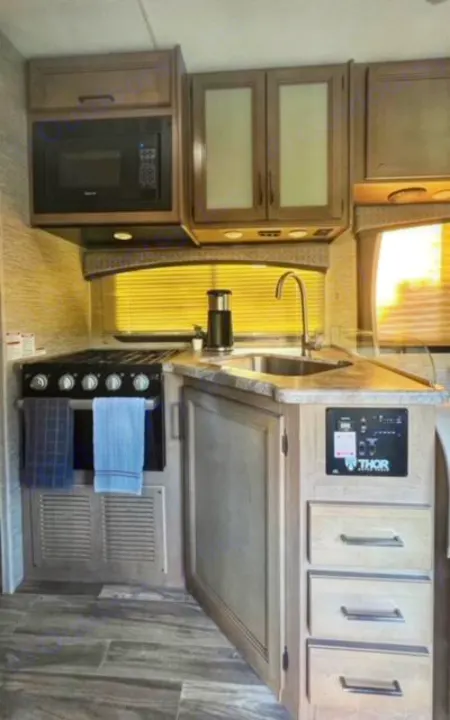 RV rental's inviting kitchen area, complete with microwave, stove, sink, and light wood cabinets.. Thor Four Winds 2022