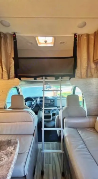 Spacious RV rental interior with an overhead bunk, ladder access, and a view of the front cab from the living area.. Thor Four Winds 2022