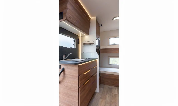 Modern RV rental interior: kitchen with sink, wooden cabinets, and bunk beds visible, offering compact comfort.. Pilote P696S 2025