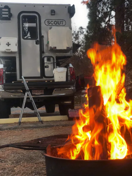 Experience the outdoors! This RV rental features a cozy campfire blazing brightly, set beside a silver truck camper for adventure.. Dodge Dodge Bighorn 3500 Heavy Duty Pu 2005