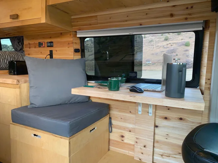 This RV rental camper van features a comfortable interior workspace with a laptop, desk, and scenic mountain views.. RAM Promaster 2500 159wb 2018