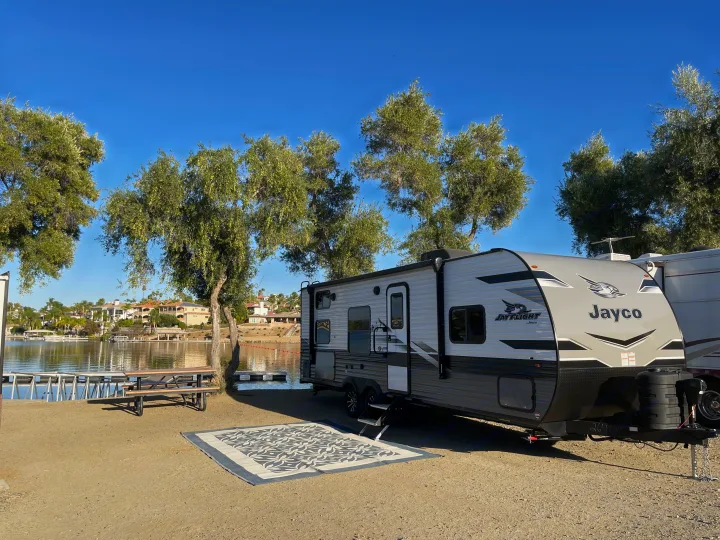 Serene lakeside RV rental: A modern Jayco travel trailer parked next to a lake with a picnic table for an outdoor adventure.. Jayco Jay Flight 2024
