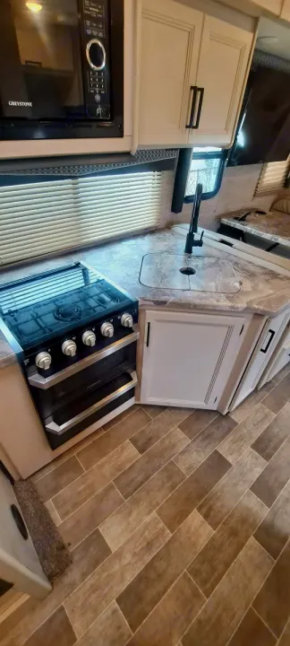 RV rental kitchen: modern interior with microwave, stove, sink, sleek cabinets, and wood-look flooring.. Thor Chateau 2021