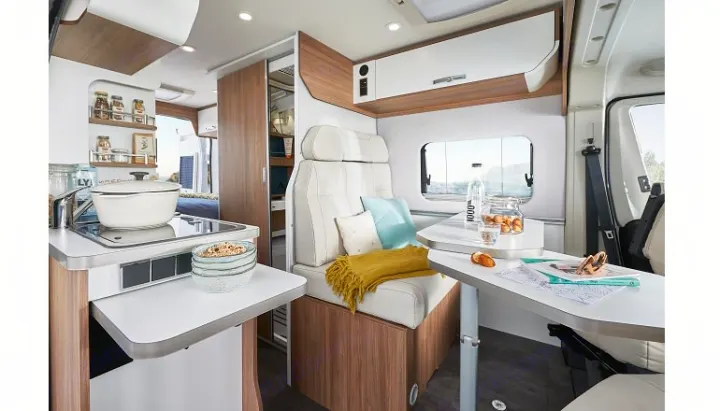 Bright, modern RV rental interior featuring a compact kitchen with stove, and a comfortable dining/seating area. Ideal for travel.. Pilote V600 Toit relevable 2023