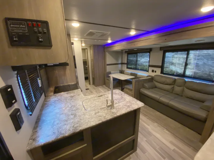 Experience comfort in this modern rv rental's spacious living area, featuring a kitchen island, dinette, and cozy sofa with ambient blue lighting.. Keystone Crossroads Zinger 2021