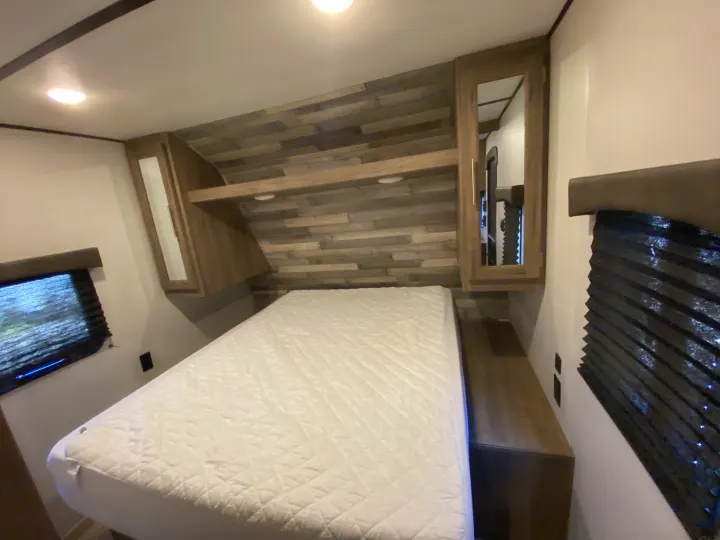 Bright RV rental bedroom features a comfy bed, stylish wood accents, mirrored cabinets, and windows with blinds.. Keystone Crossroads Zinger 2021